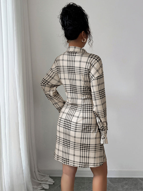 Person wearing a plaid dress standing against a white wall with curtains.
