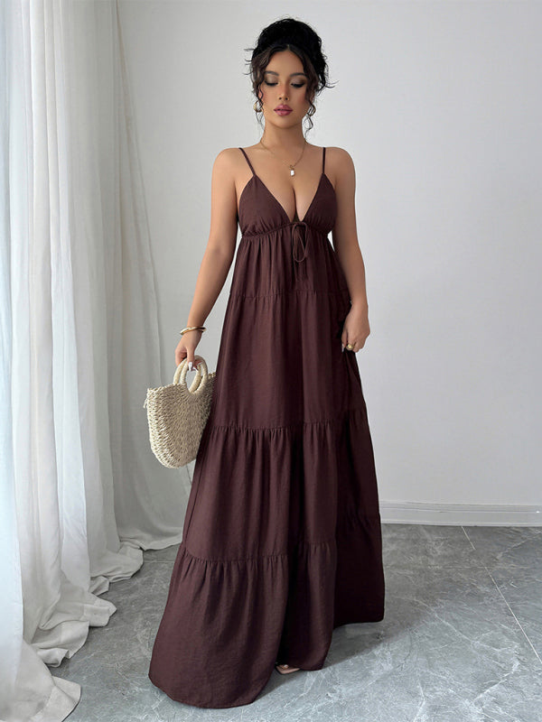 Woman wearing a long brown dress holding a straw bag against a neutral background