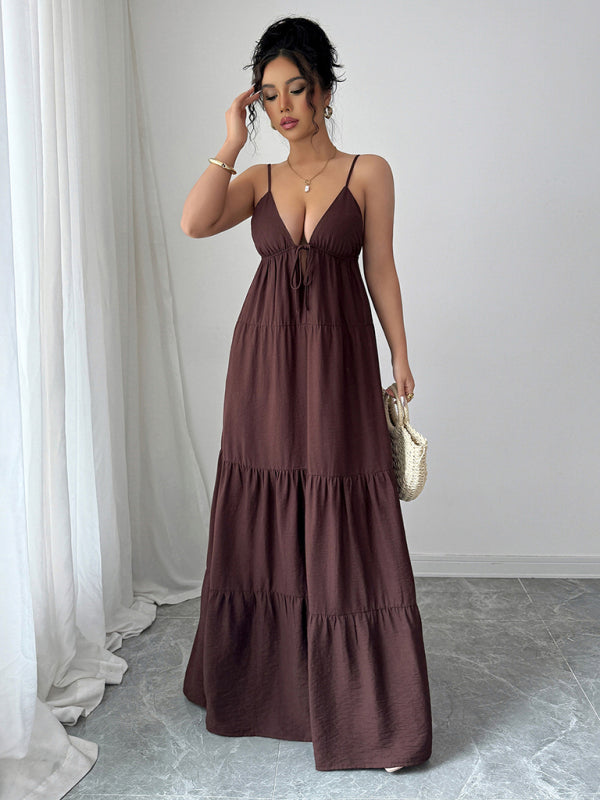Woman wearing a brown maxi dress standing against a white curtain.
