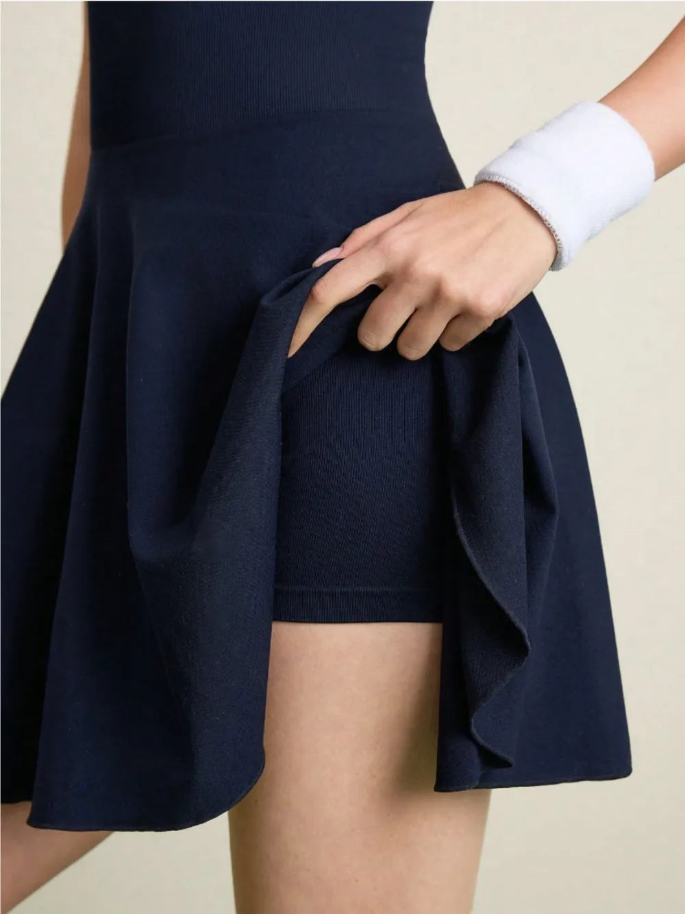 "Front and back view of women's navy tennis dress featuring halter neck design, flared skirt, open back, and coordinating navy headband with white stripes."

