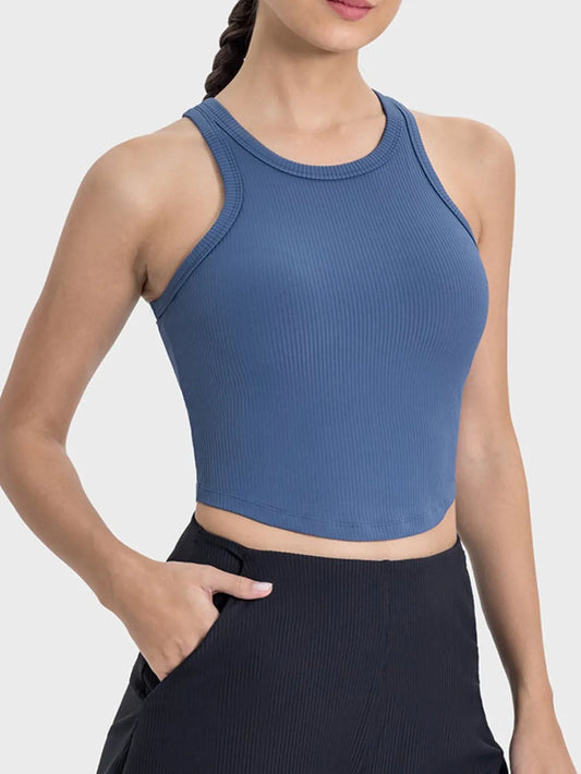 "Dusty blue ribbed crop top with racerback design worn by model with braided hair, paired with black athletic bottoms."
