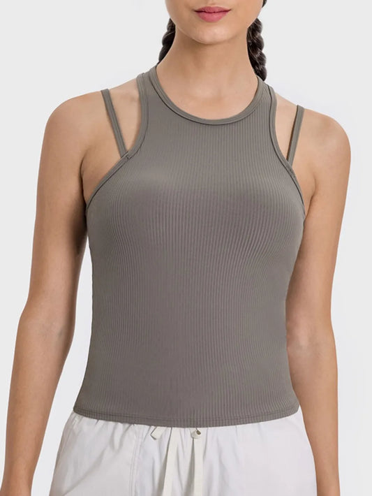 "Taupe ribbed tank top with double shoulder straps and round neckline, shown on model with braided hair and white bottoms."
