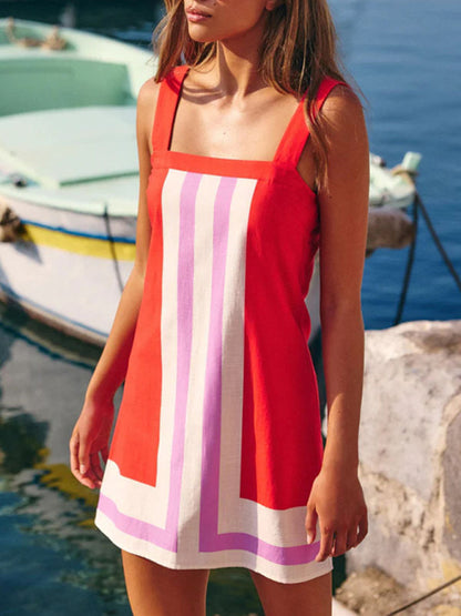 Woman wearing a red dress with white and purple stripes by a body of water with boats.