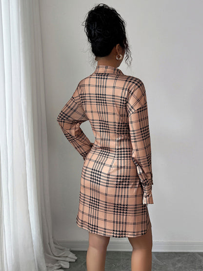 Person wearing a plaid dress standing against a white wall.