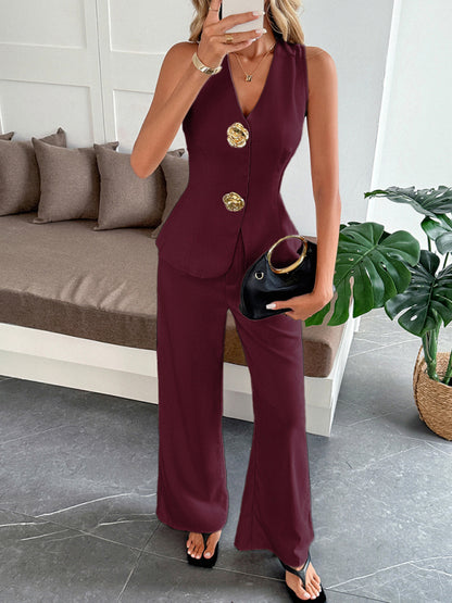 Woman in a burgundy suit with gold buttons holding a black clutch in a living room.